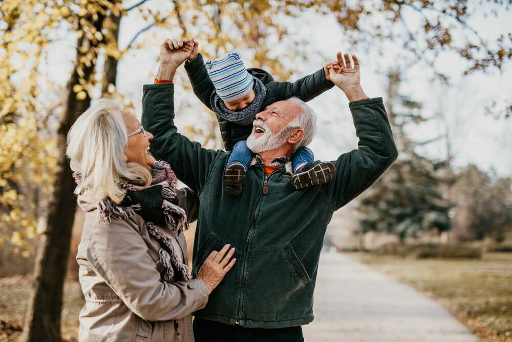 Grandparents lifting a grandchild on a tree-lined autumn path